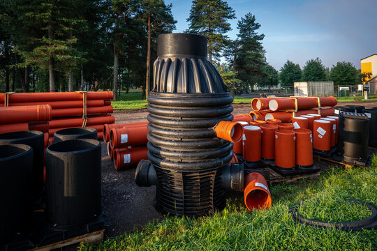 Large Black Manhole Chamber Among Orange Sewer Pipes in Outdoor Storage Yard