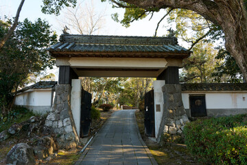 Fototapeta premium KITSUKI, OITA, JAPAN - FEBRUARY 17, 2025: Traditional Japanese gate with stone walls and paved path leading into Shiroyama Park at Kitsuki Castle in Oita Prefecture, Kyushu.