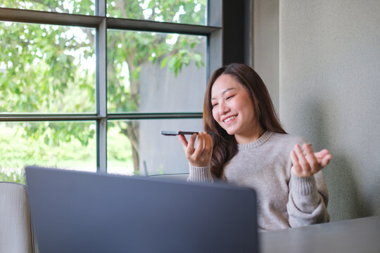 A woman holding smart phone and using voice messaging, talking with ai assistant for Artificial intelligence concept while working on laptop
