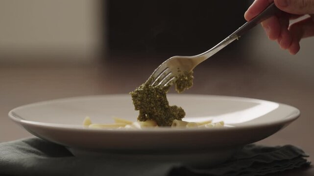 Slow motion making pesto penne pasta with mozzarella and tomatoes in deep plate closeup