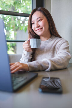 Vertical portrait image of a woman drinking coffee while working on laptop computer