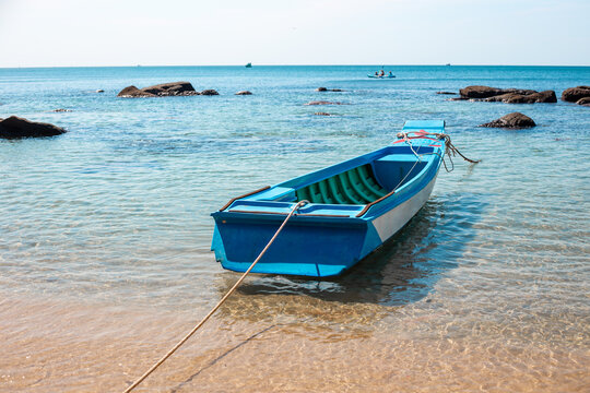A small blue wooden boat anchored on a sandy beach in calm turquoise ocean water. tropical island travel, idyllic beach getaway, summer vacation.