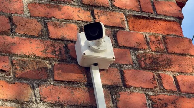 A modern CCTV surveillance camera mounted on a weathered red brick wall, symbolizing security, monitoring, and urban safety. Ideal for footage related to home security, business protection, privacy.