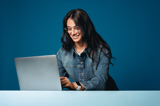 Smiling woman uses a laptop for study in a blue studio