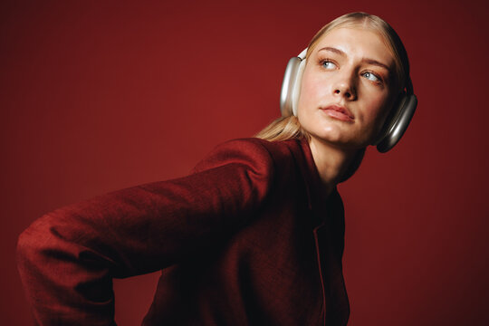 Headphones frame the woman in a red studio portrait with fashion styling