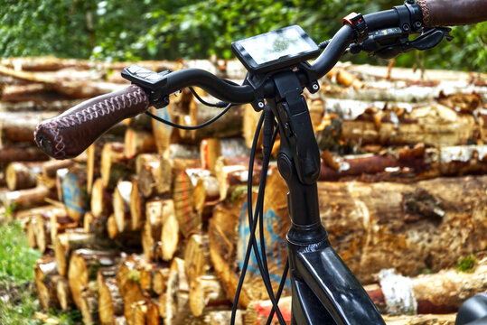 E bike handlebars with leather grips and digital display against stacked timber logs in a forest