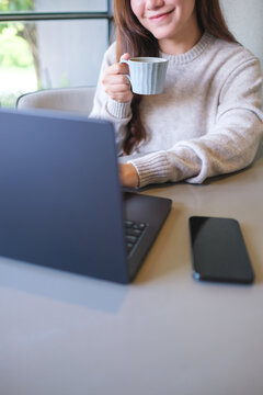 Vertical closeup image of a woman drinking coffee while working on laptop computer