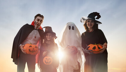 Obraz premium Happy Family in Halloween Costumes Celebrating Outdoors at Sunset