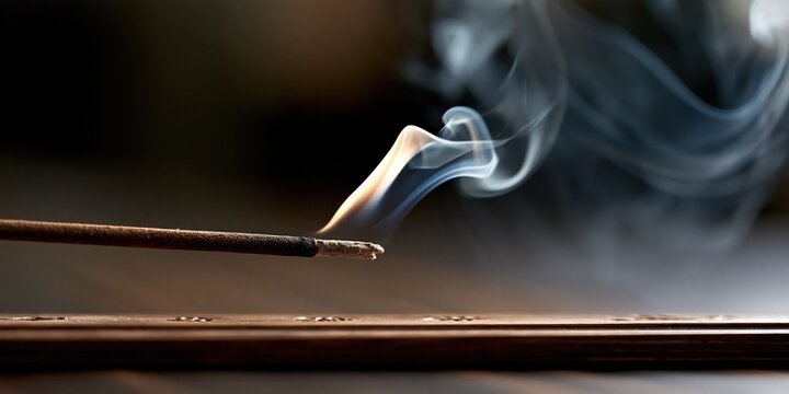 Fragrant smoke curls from a glowing incense stick held on a wooden stand in a dim quiet room