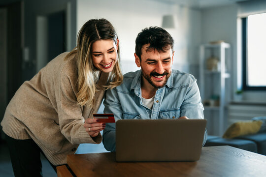 Smiling couple using credit card and laptop at home, representing fintech innovation digital finance