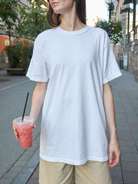 Woman in white t-shirt and shorts holding a pink drink on a city street