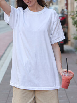 Woman in white t-shirt and beige shorts holding a pink drink outdoors