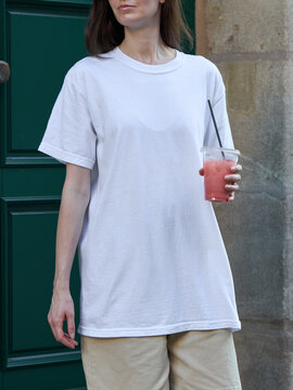 Woman in a white t-shirt holding a pink drink outdoors