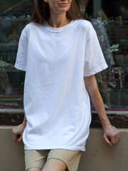Woman wearing a plain white t-shirt and beige shorts leaning against a wall © 4Max