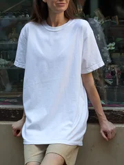 Woman wearing a plain white t-shirt and beige shorts leaning against a wall © 4Max