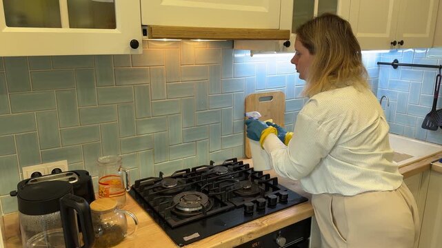 Woman in rubber gloves cleaning integrated range hood over gas stove in kitchen