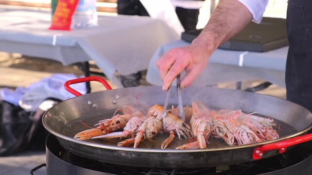 Outdoor chef cooking fresh shrimp in a large pan at a food festival. 