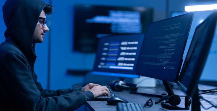 Hacker male wearing hoodie typing on computer keyboard in dark room, Concept of cybersecurity, cybercrime, software engineering, dark web, data breaches and modern digital network protection