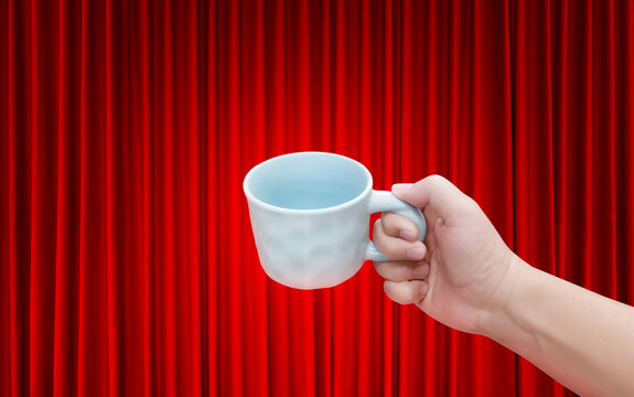 An empty white ceramic coffee cup is in a man's hand, with a red curtain as a background.