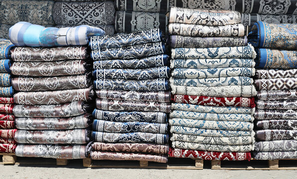 Stacks of traditional Uzbek kurpacha mattresses with decorative fabric patterns displayed for sale. Colorful quilted bedding traditionally used in Central Asian homes for seating, sleeping, home decor