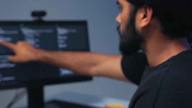 Portrait of Professional Indian Male Software Developer, Computer Programmer working on computer typing on keyboard, writing code and Pointing at Monitor, Reviewing and Checking Code on Screen.