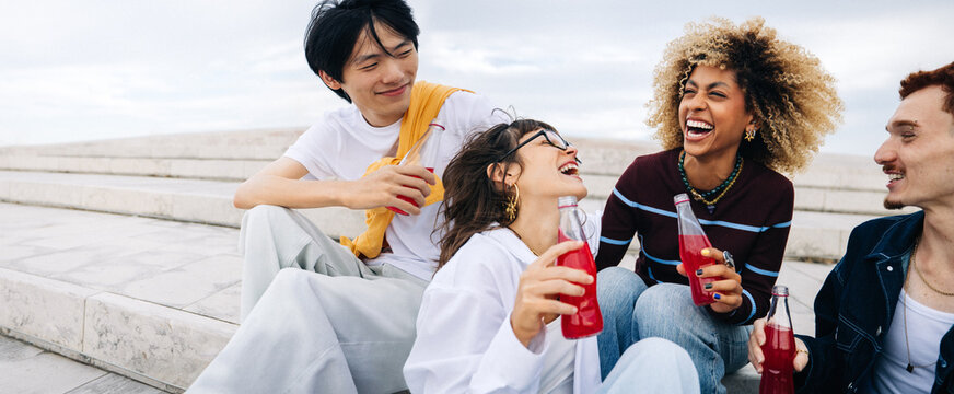 Friends laughing together while drinking soda on steps