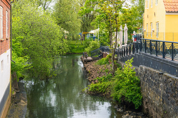Water shaped town greenery follows a calm urban waterway between buildings and vegetation in Ribe, Denmark, for sustainable towns, local environment and slow travel themes. © Nimbus Works