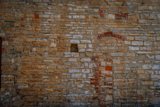 Textured stone wall with various shades of beige and brown, featuring a small window and brick arch in a historical setting in Bergamo
