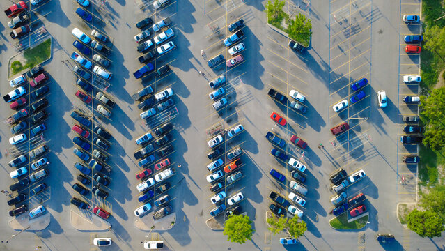 Outer suburban commercial precinct features structured stalls framing commuter automobiles. Drivers maneuver occupied aisles past pedestrian crosswalks near storefronts in San Antonio, TX