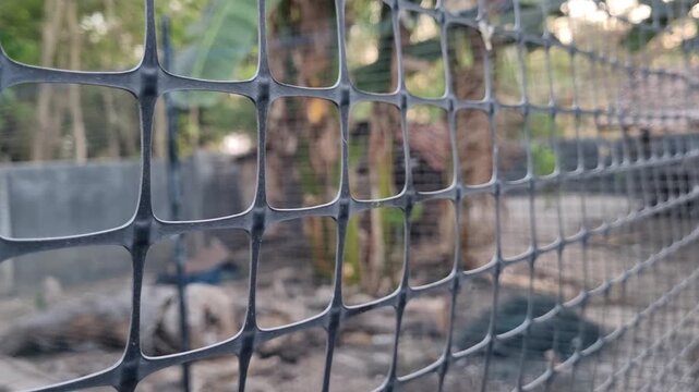 Close up of black plastic mesh fence grid pattern in blurred outdoor garden background