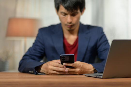 Young Man Using Smartphone in Workspace with Laptop and Interior Background