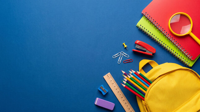 Colorful school supplies, yellow backpack, notebooks, colored pencils, and ruler on a dark blue background with copy space for back to school concept.