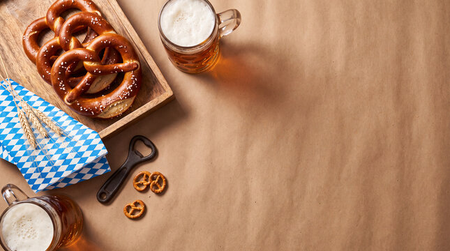 Oktoberfest flat lay with traditional pretzels, foamy beer mugs, and blue-white checkered napkin on a rustic background. Perfect for celebration themes.