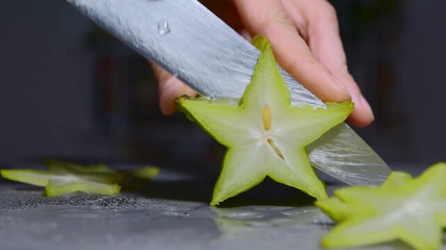 Close-up of a hand slicing a juicy starfruit into star shapes, revealing its delicate texture and edible seeds