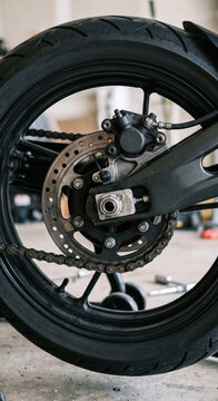 Rear motorcycle wheel with ventilated brake disc, caliper, tire, and swingarm, photographed with clear materials, realistic texture, and precise mechanical detail.