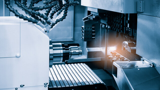 CNC machine with metal components. Cylindrical workpiece sits on the table. Orange tool holder is visible. Industrial manufacturing equipment shows precise work