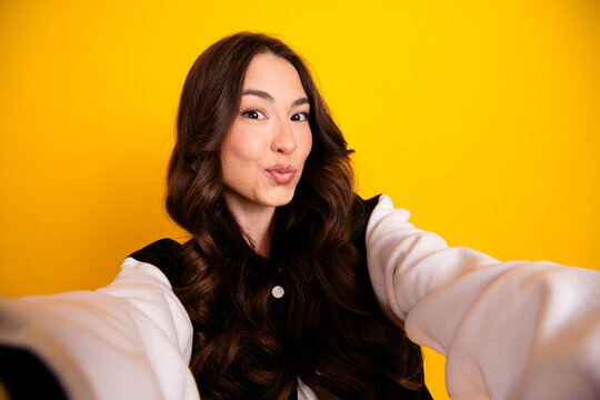 Young woman taking a playful selfie puckering her lips with long hair against a bright yellow background