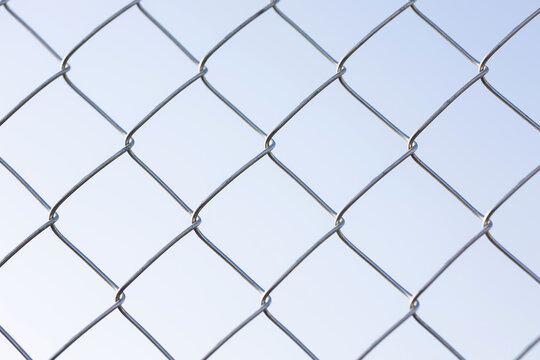 Chain link fence forming a metal mesh pattern against a clear blue sky
