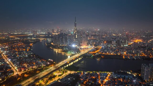 Landmark 81, Ho Chi Minh City skyline at night, aerial view of illuminated skyscrapers along Saigon River with traffic light trails, Vietnam.