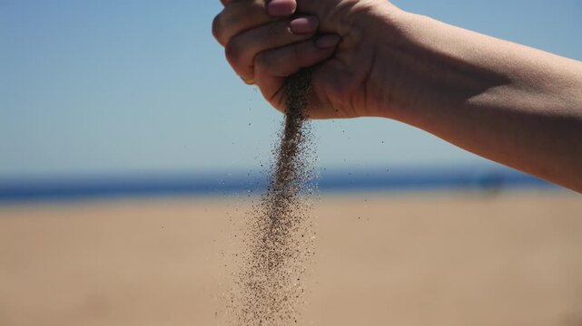 Close up of a hand letting sand fall through fingers on a sunny beach. Slow motion summer travel relaxation and vacation concept. High quality 4k footage