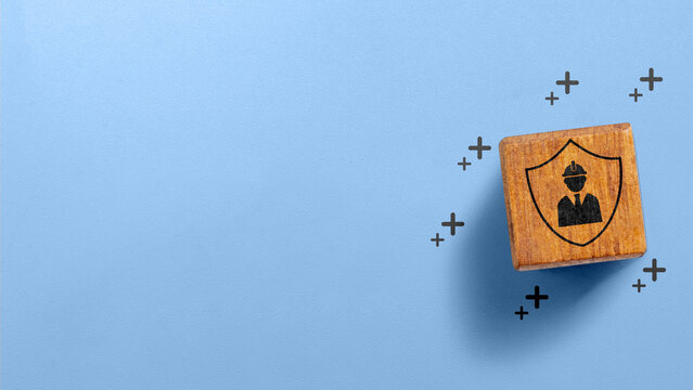 Wooden block showing a worker safety and protection icon on a blue background with copy space. Occupational safety concept