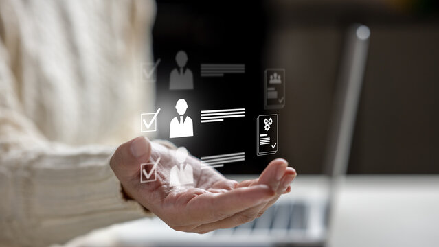 Female hand holding virtual HR icons representing recruitment, candidate selection, and user profiles with a laptop in the background. HR Recruitment concept