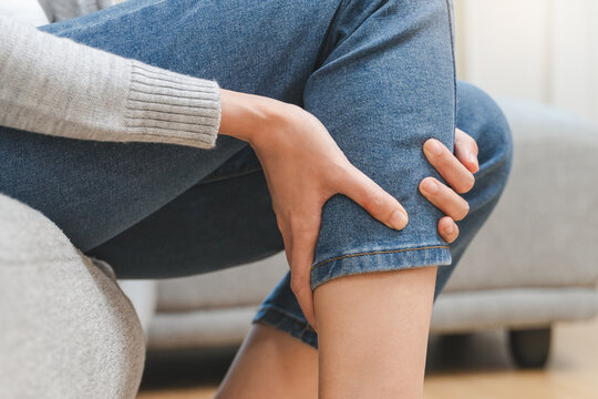 Woman get cramp on the leg sitting on sofa