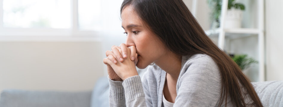 Unhappy anxiety young Asian woman covering her face with pillow on the cough in the living room at home