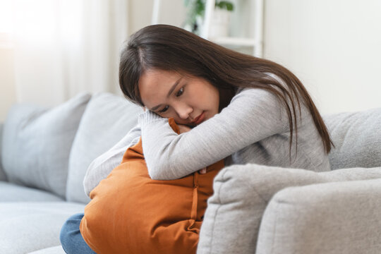Unhappy anxiety young Asian woman covering her face with pillow on the cough in the living room at home