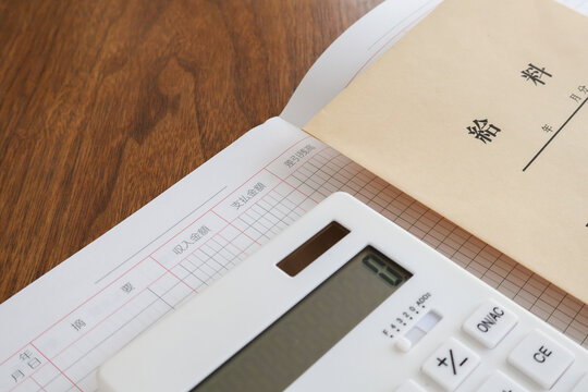 木製机の上の白い電卓と給料袋と家計簿／家計管理イメージ