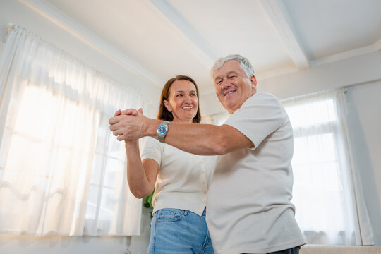 Cheerful senior couple dancing together at home, Loving elderly couple enjoying time and dancing in living room, Happy mature husband and wife spending time together at home