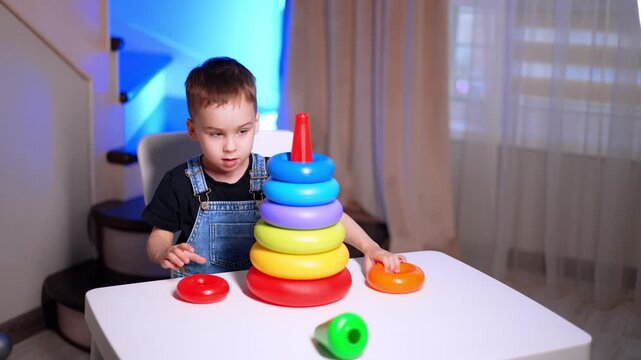 Boy arranging rings on colorful stacking toy. A tall tower stands on the table as he touches an orange piece nearby.
