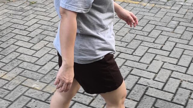 Someone is out for a casual walk as a form of exercise, dressed in casual attire. Viewed from the side, the person is walking along a paved path, featuring a herringbone pattern.Jogging video 4k 60fps