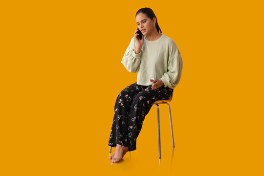 Indian girl speaking with someone on smartphone while sitting on chair